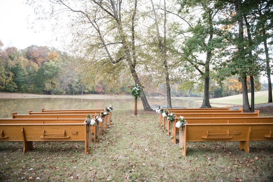 Lakeside ceremony setup with wooden pews at Heyward Manor